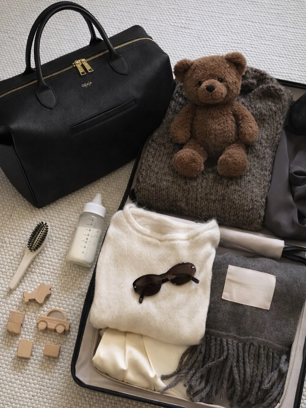 Un sac ALBA noir ouvert, prêt pour la journée : doudou, biberon, vêtements