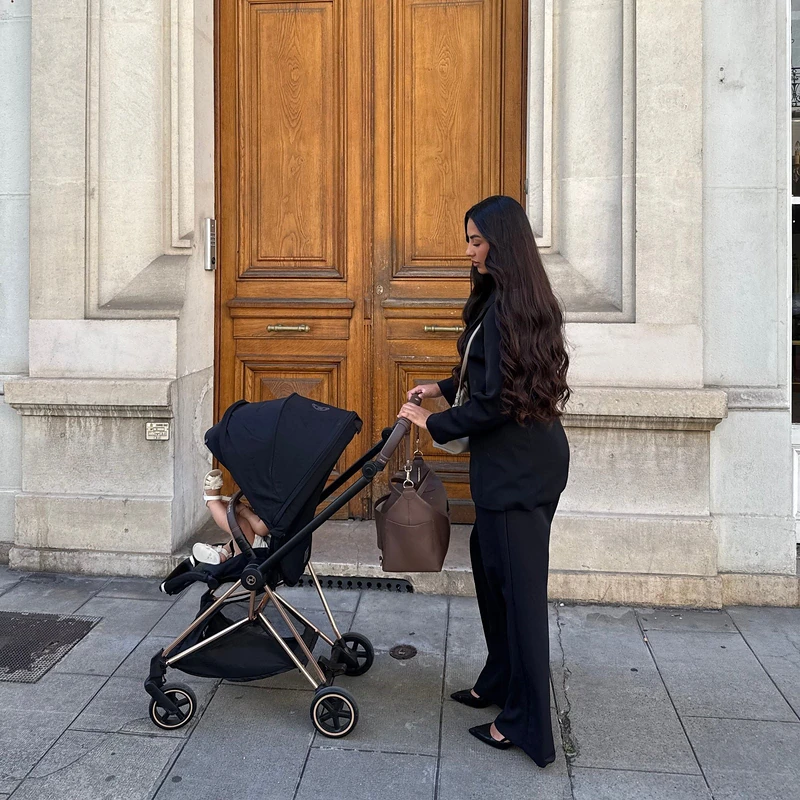 Une maman sort par une porte cochère avec la poussette, le sac ALBA accroché