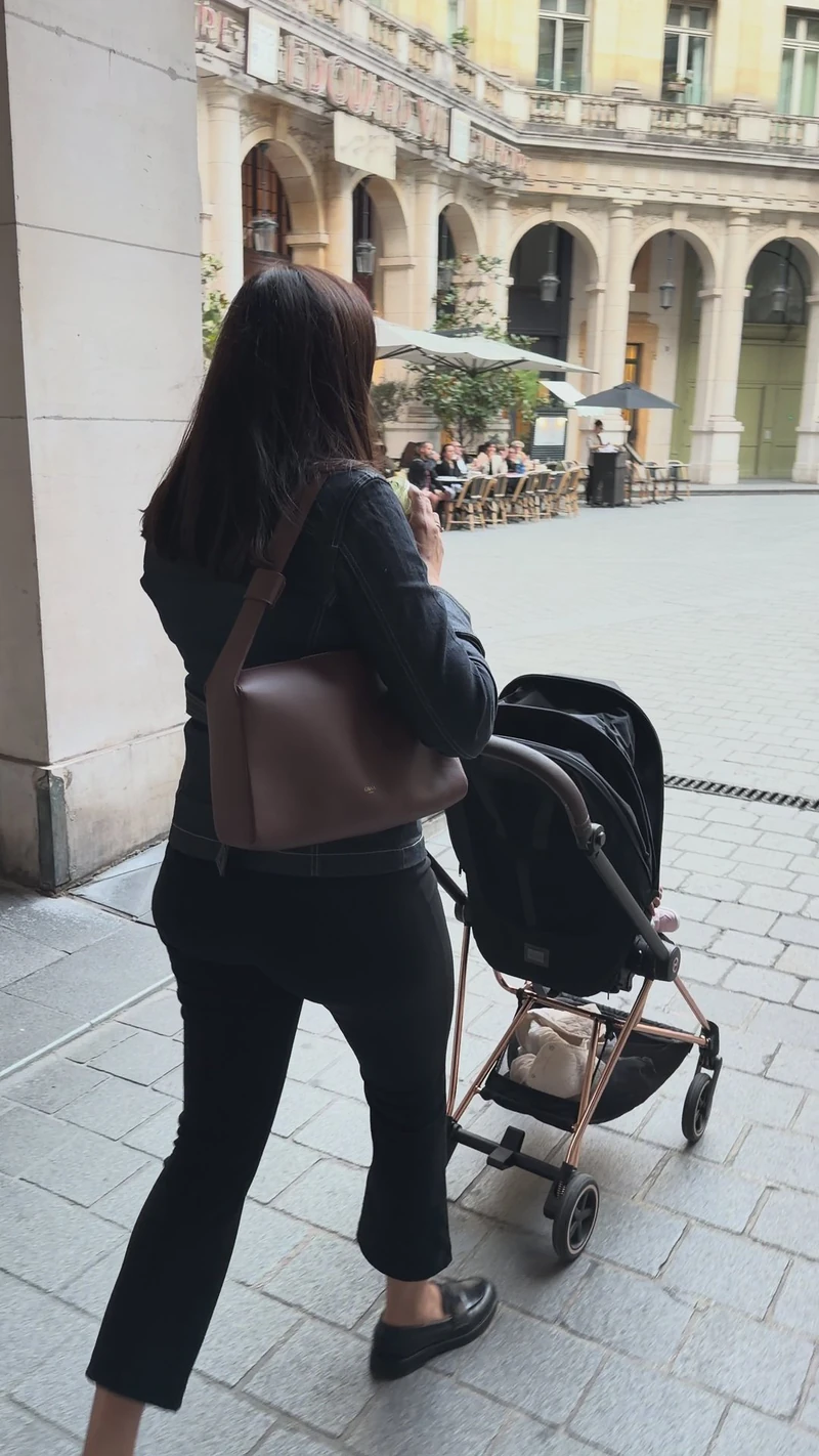 Une maman se promène avec la poussette dans une rue de Paris, son sac ALBA brun à l’épaule